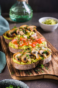 Sandwiches with avocado, fried champignons, tomatoes and herbs on rye bread on a board vertical view