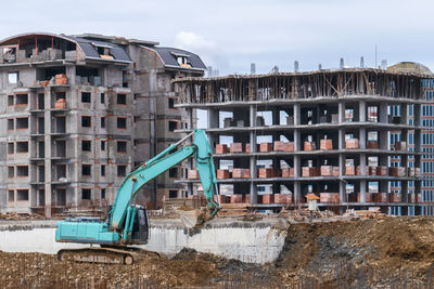 Excavator with bucket on construction site against background of houses under construction