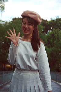 Portrait of happy young woman waving while standing on bridge