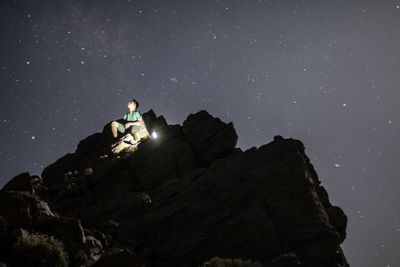 Low angle view of man sitting on rock formation at night