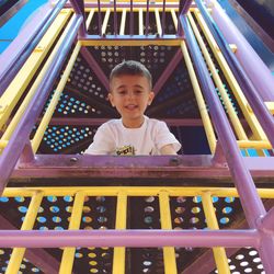 Low angle portrait of boy standing in play equipment at playground