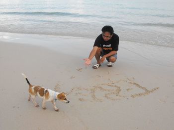 Man with dog crouching at beach