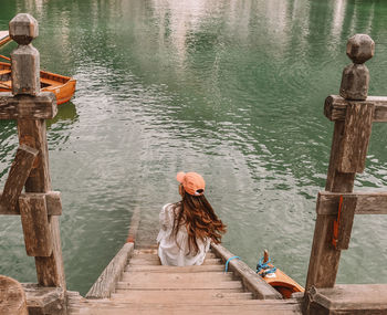Rear view of woman sitting on pier at lake 