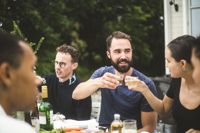 Man and woman toasting drinks while enjoying dinner party with friends in backyard