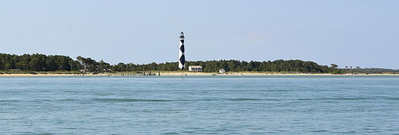 Lighthouse by sea against clear sky