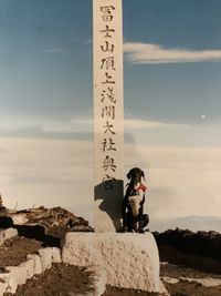 Young woman standing on rock against sky