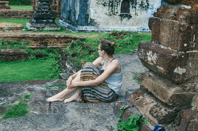 Woman looking away while sitting by built structure