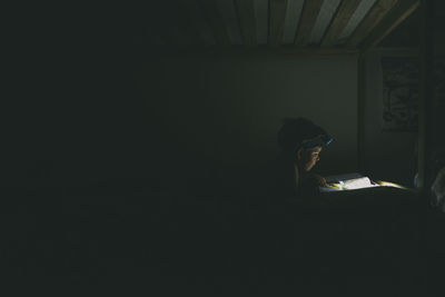 Boy using headlamp while reading book in darkroom