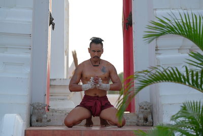 Portrait of shirtless man kneeling on steps outside temple