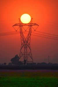 Silhouette electricity pylon on land against orange sky at sunset