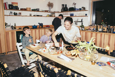 Smiling mother during dinner time with sons sitting at dining table in kitchen