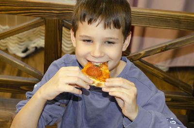 Boy eating pizza. child closed his eyes in pleasure and takes a bite of pizza piece holding it aloft
