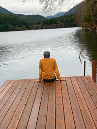 Rear view of man sitting on pier over lake