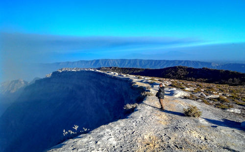 High angle view of man standing on cliff against blue sky