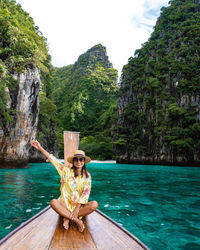 Man sitting on rock by sea against mountain