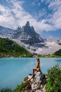 Man sitting on rock by lake against sky