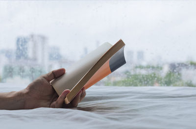 Hand holding a book that reading on bed when rainy day. stay home and relaxing concept