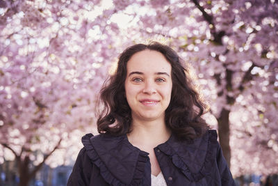 Portrait of young woman standing under cherry blossom