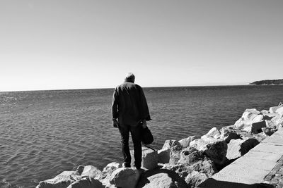 Rear view of man looking at sea against clear sky