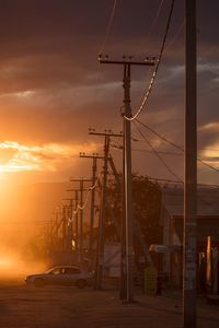 Electricity pylon by road against dramatic sky during sunset