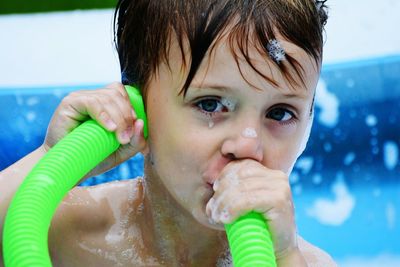 Portrait of playful boy with green pipe while taking a bath