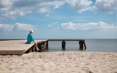 Old woman at the beach, sitting at the dock looking at the horizon.