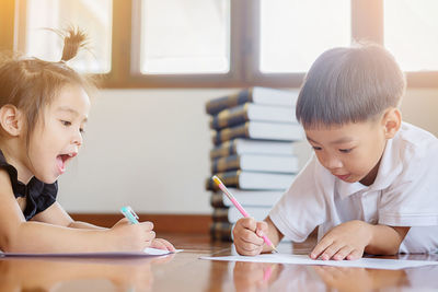 Close-up of siblings writing while lying on floor at home