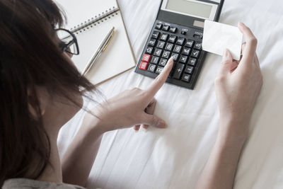 Close-up of woman using calculator on bed 