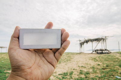 Cropped hand of man holding wooden block against sky