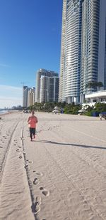 Rear view of man walking on beach against buildings in city