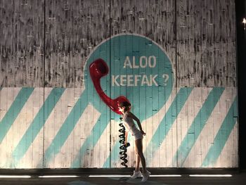 Full length side view of woman standing by wall in city at night