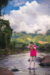 Full length of woman standing on rock amidst river against sky