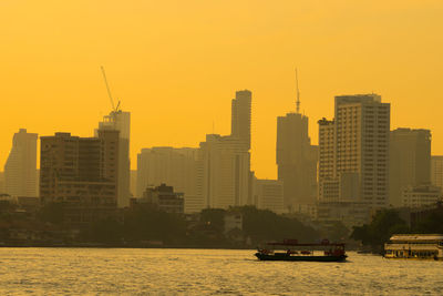 Buildings by river against sky during sunset