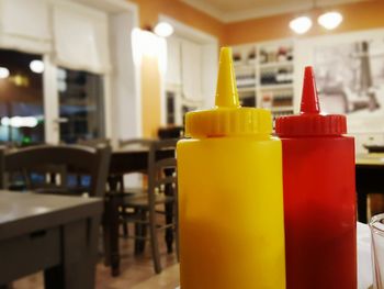 Close-up of red and yellow bottle on table at illuminated restaurant
