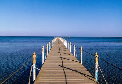 Pier over sea against clear blue sky