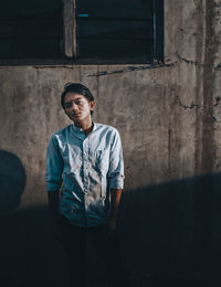 Portrait of young man standing against wall in building