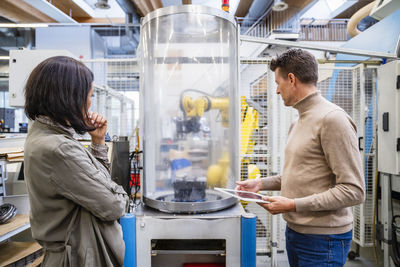 Businessman holding and businesswoman analyzing machine in industry