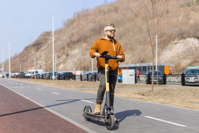 Rear view of man riding push scooter on road