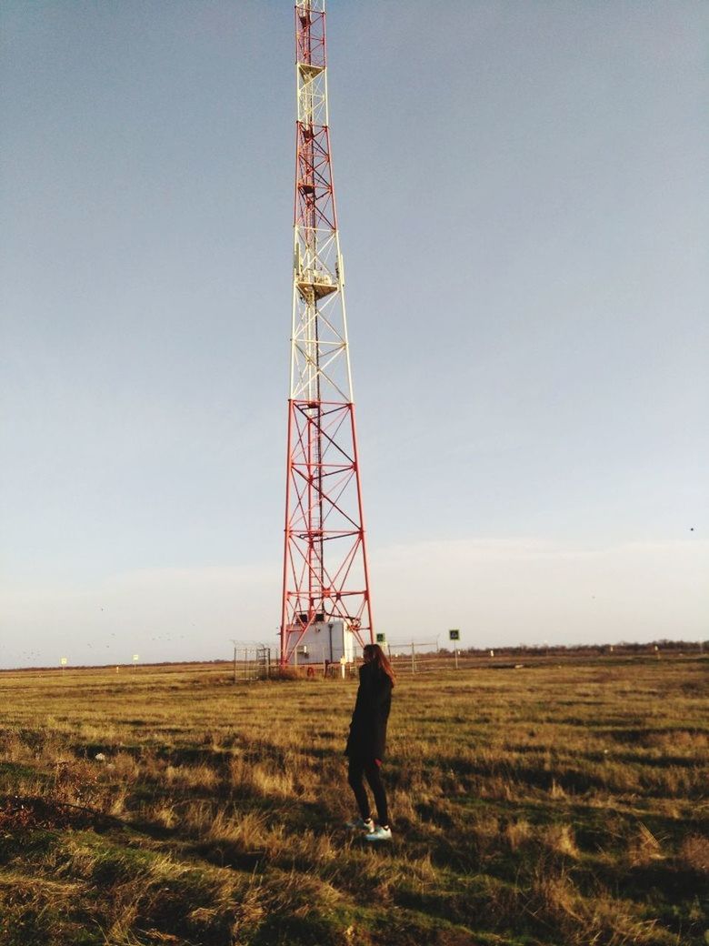 sky, field, land, nature, real people, landscape, technology, tower, day, horizon over land, environment, built structure, one person, grass, full length, connection, architecture, outdoors, tall - high, global communications