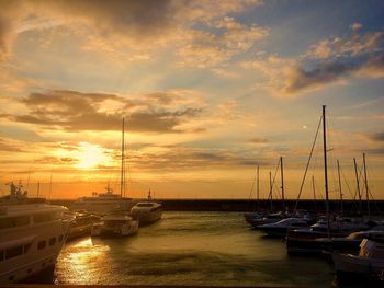 Sailboats moored on harbor against sky during sunset