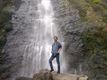 Full length of young man standing against waterfall