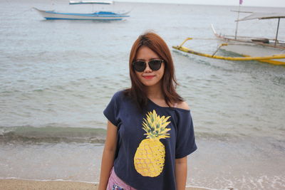 Young woman wearing sunglasses standing at sea shore