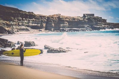 Woman with surfboard standing at beach