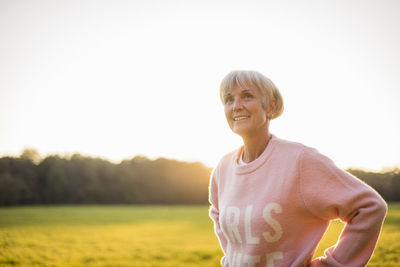 Smiling senior woman standing on rural meadow at sunset