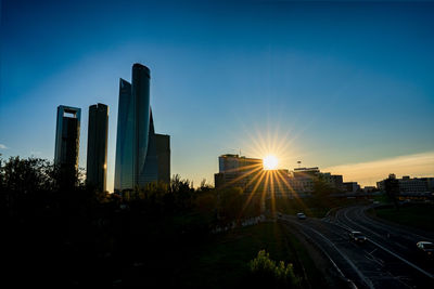 Road by buildings against sky during sunset