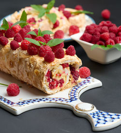 Baked meringue roll with cream and fresh red raspberry on a black wooden board, delicious dessert