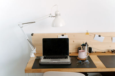 From above composition of modern portable netbook with black screen placed on wooden desk near cup and eyeglasses in light office