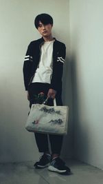 Portrait of young man holding shopping bag while standing against wall