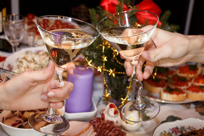 Cropped hands of man and woman toasting martini glasses at dining table