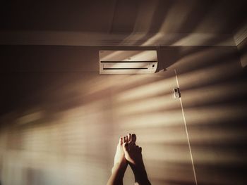 Low section of woman with feet up against air conditioner on wall at home